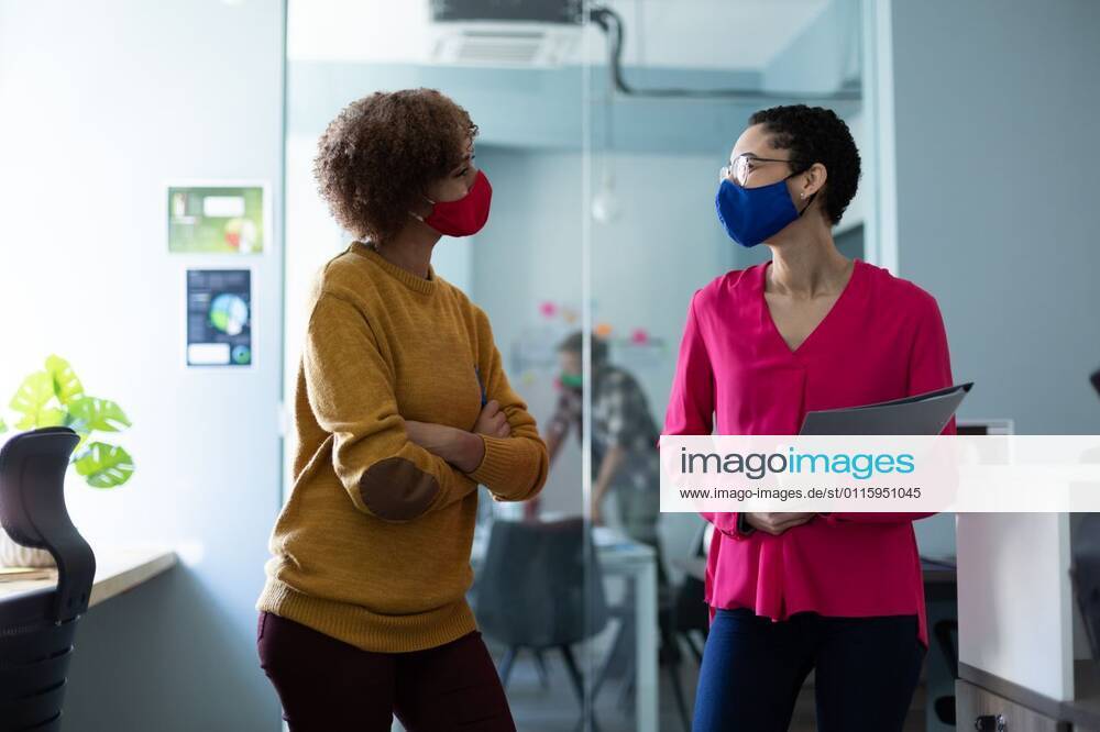  wearing masks talking in an office Two mixed race women wearing masks talking in an office. hygiene